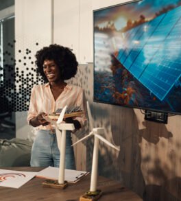 Portrait of smiling multicultural female environmentalist standing at boardroom with solar panels prototype in hands and presenting innovative green technology. Diverse ecology expert having speech